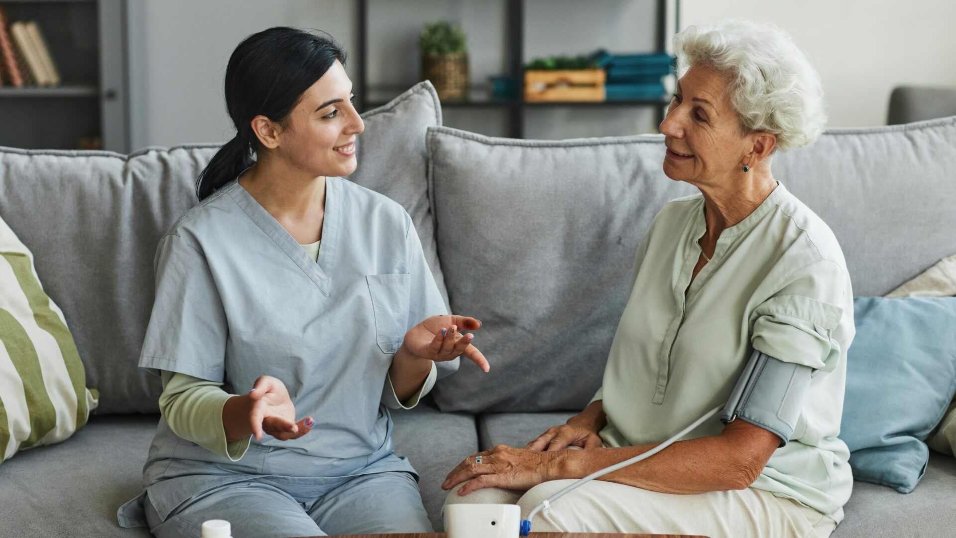 Adult healthcare worker talking to woman on couch.