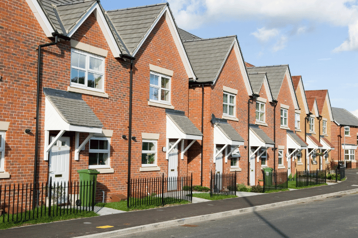 image of a row of red brick houses with black picket fences white windows lined along a main road